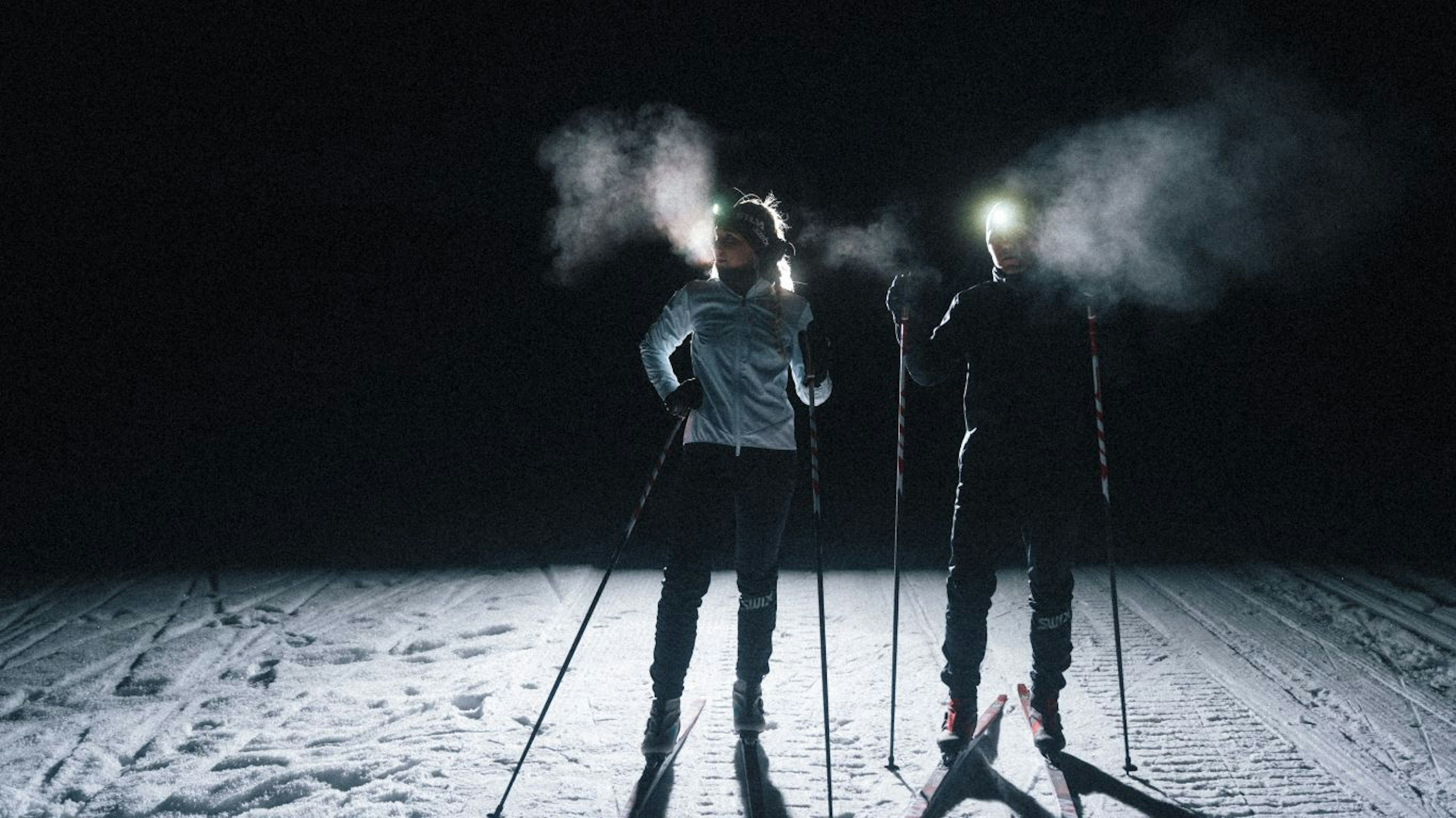 Two people skiing at night-time with headlamps